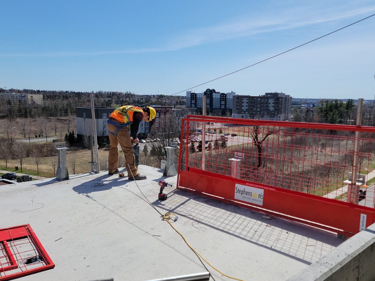 A Keep Clean worker at the edge of a rooftop slab behind safety fencing